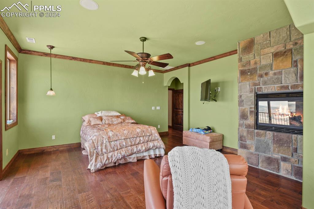 Image 21 of 50: Bedroom featuring ceiling fan, ornamental molding, a fireplace, and dark wo