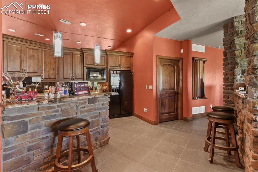 Image 30 of 50: Kitchen featuring light stone counters, black appliances, light tile floors