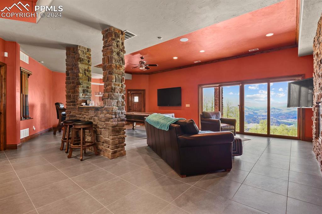 Image 31 of 50: Tiled living room with ceiling fan and decorative columns
