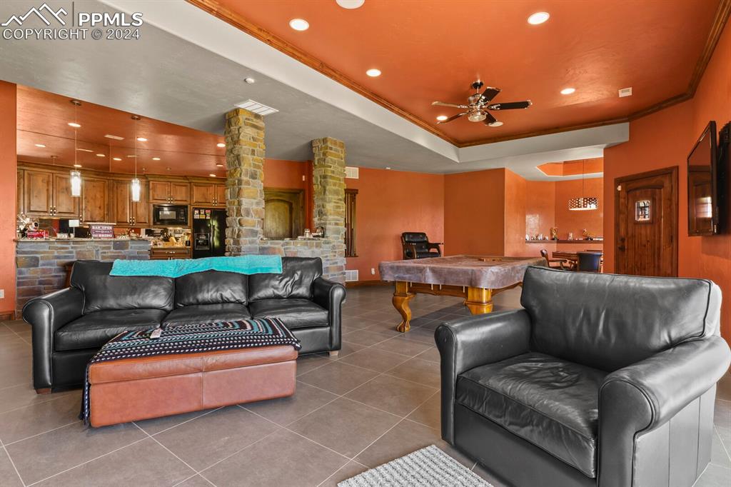 Image 32 of 50: Living room with ceiling fan, decorative columns, a raised ceiling, tile fl