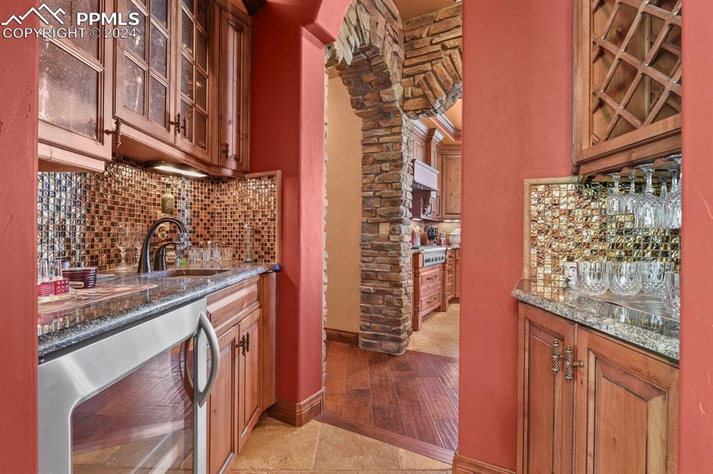 Image 8 of 50: Kitchen with dark stone counters, beverage cooler, sink, tasteful backsplas