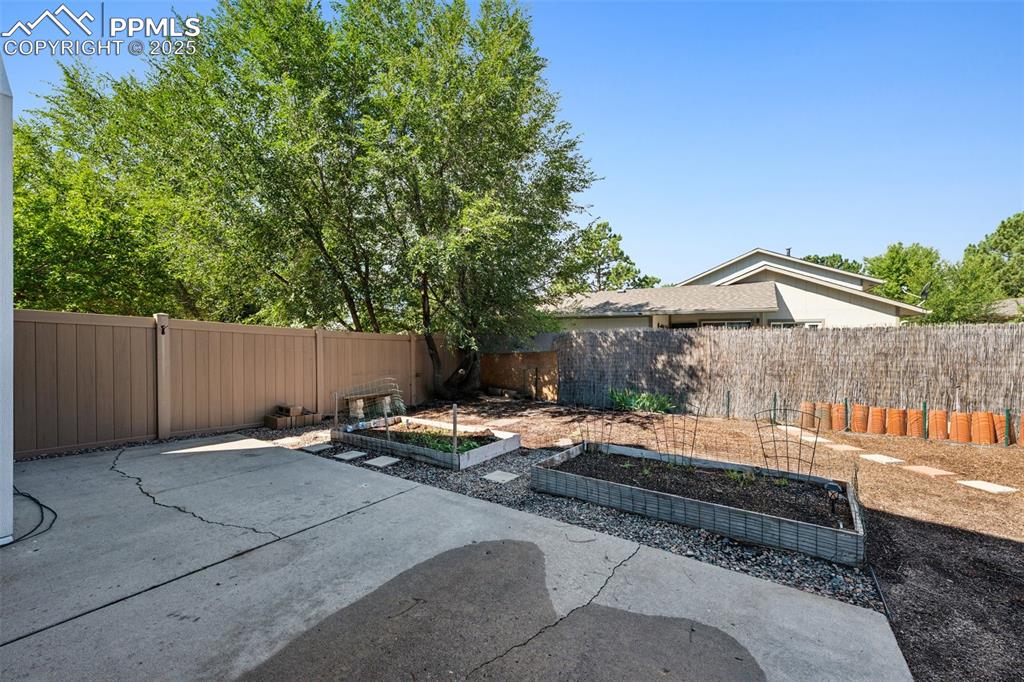 Image 34 of 35: Fenced backyard featuring a vegetable garden and a patio