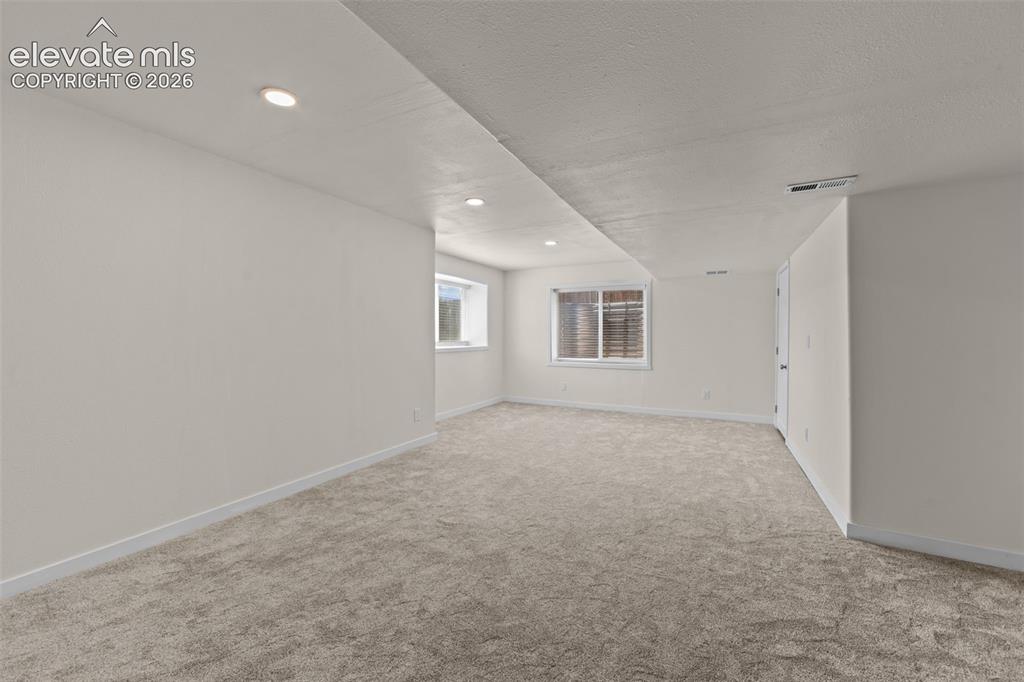 Image 24 of 33: Spacious room featuring neutral carpeting, recessed lighting, and white bas