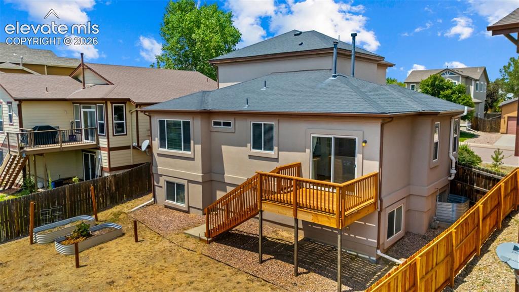 Image 29 of 33: Rear exterior featuring a wood deck with stairs to the ground level, stucco