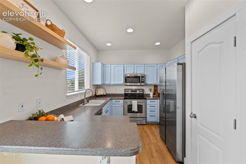 Image 7 of 33: Kitchen featuring light blue cabinetry, stainless steel appliances, wood-fi