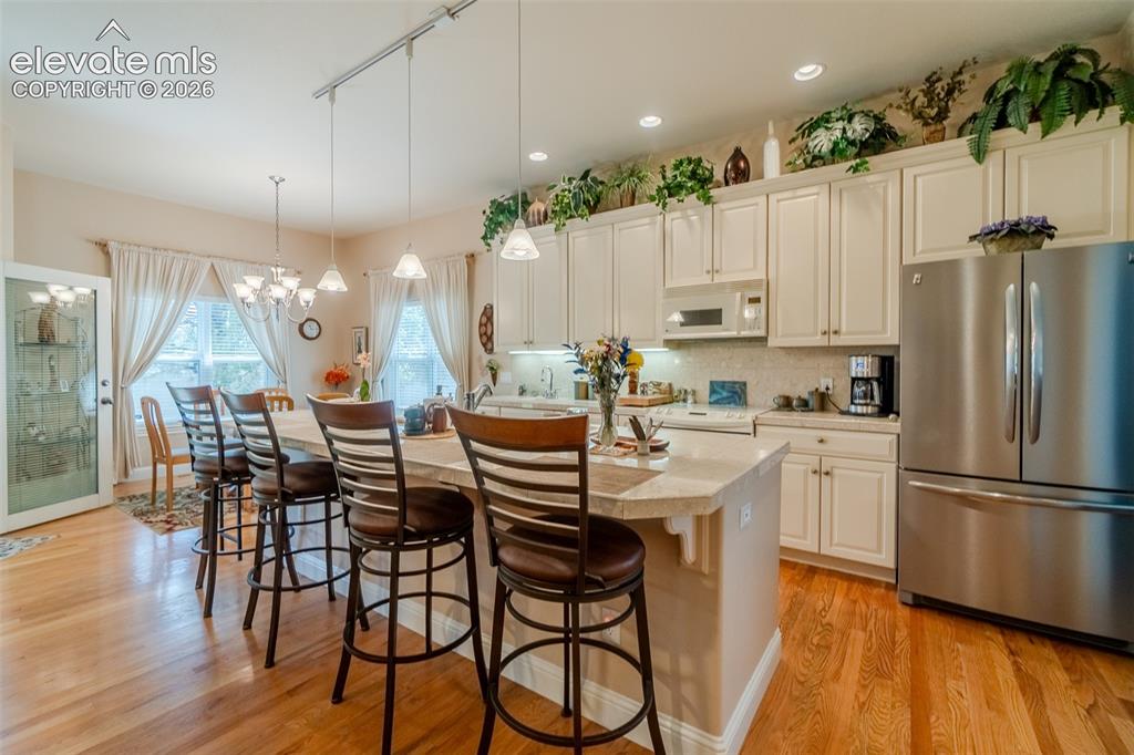 Image 11 of 47: Open-concept kitchen featuring wood-finish flooring, white cabinetry, stain