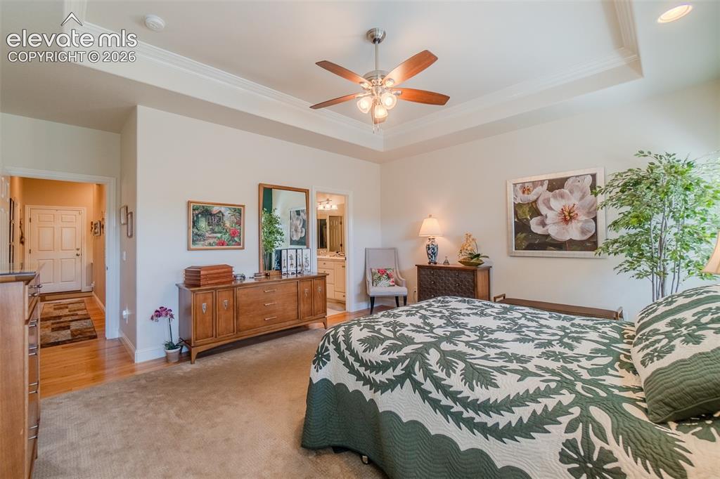 Image 14 of 47: Primary bedroom featuring a tray ceiling with crown molding, a ceiling fan