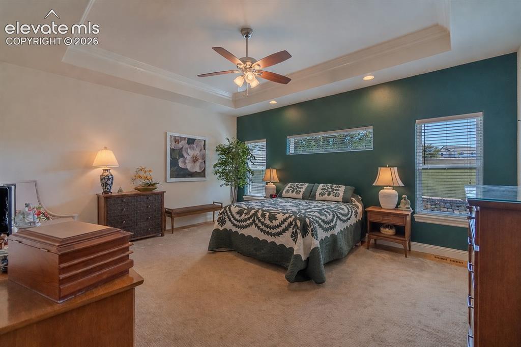 Image 16 of 47: Spacious bedroom featuring a tray ceiling with a ceiling fan, recessed ligh