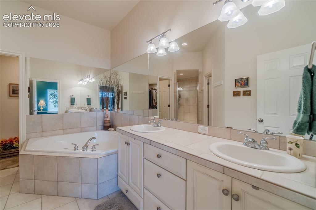 Image 17 of 47: Bathroom featuring a tiled corner soaking tub, a dual vanity with tile coun