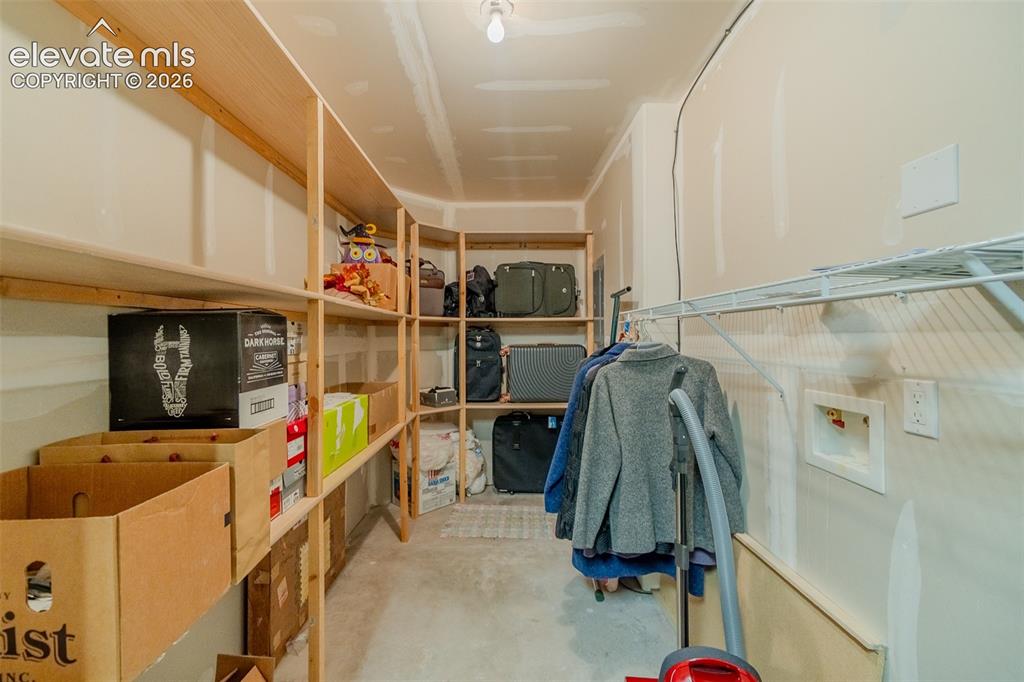 Image 44 of 47: Utility room with extensive built-in wooden shelving, concrete flooring, ov