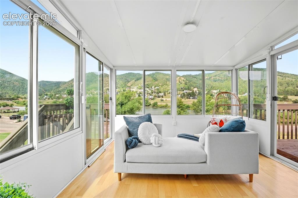 Image 19 of 49: Sunroom with expansive windows, wood-finish flooring, white walls, and a ce