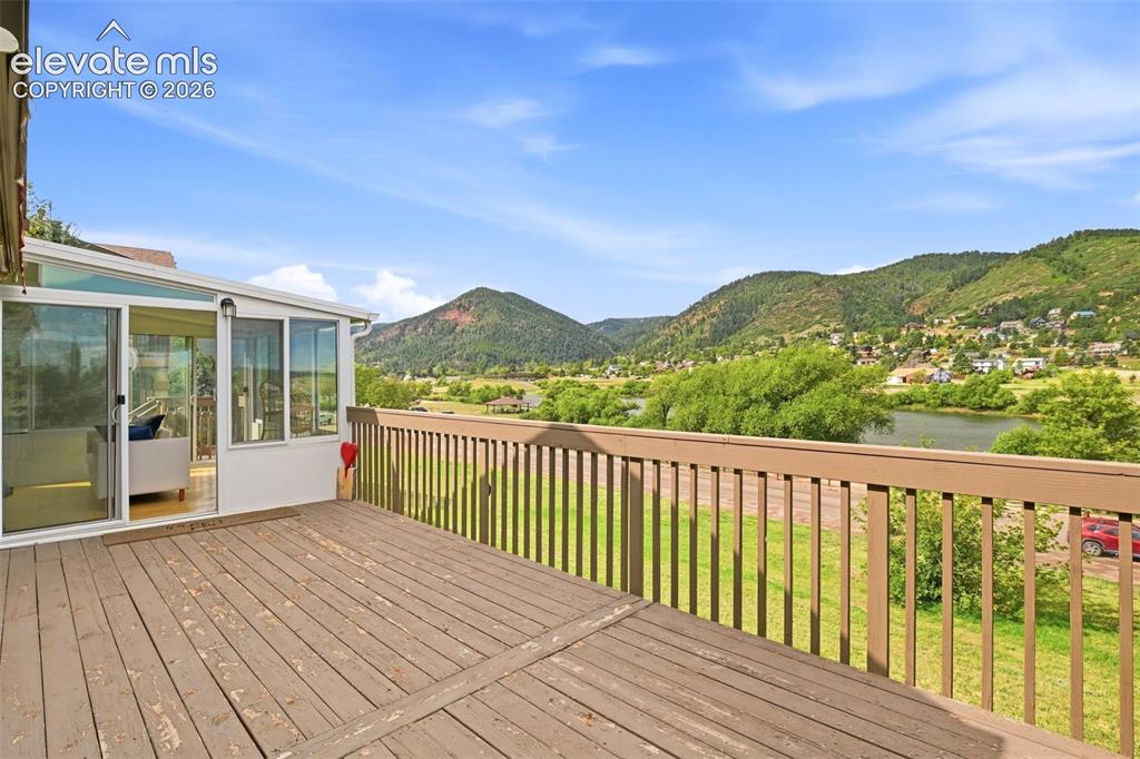 Image 24 of 49: Expansive wood-finish deck with a sunroom, featuring multiple windows and s