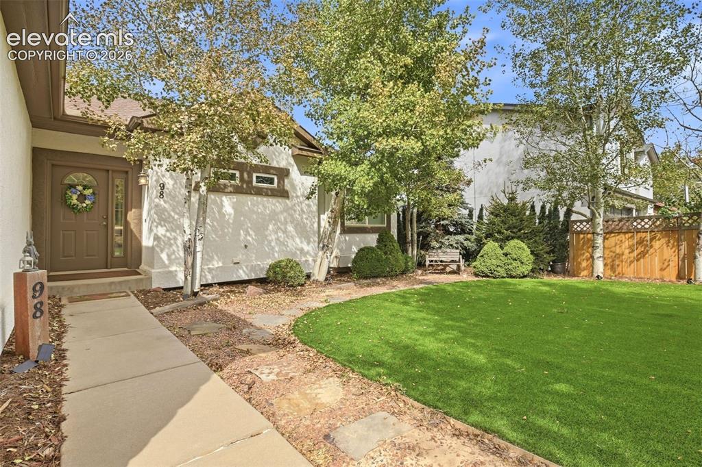 Image 3 of 49: Stucco exterior with a brown entry door, concrete walkway, stone-lined path