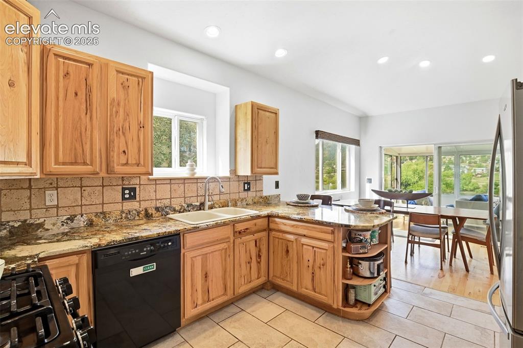 Image 32 of 49: Kitchen featuring wood cabinetry, stone countertops, a dual-basin sink, til