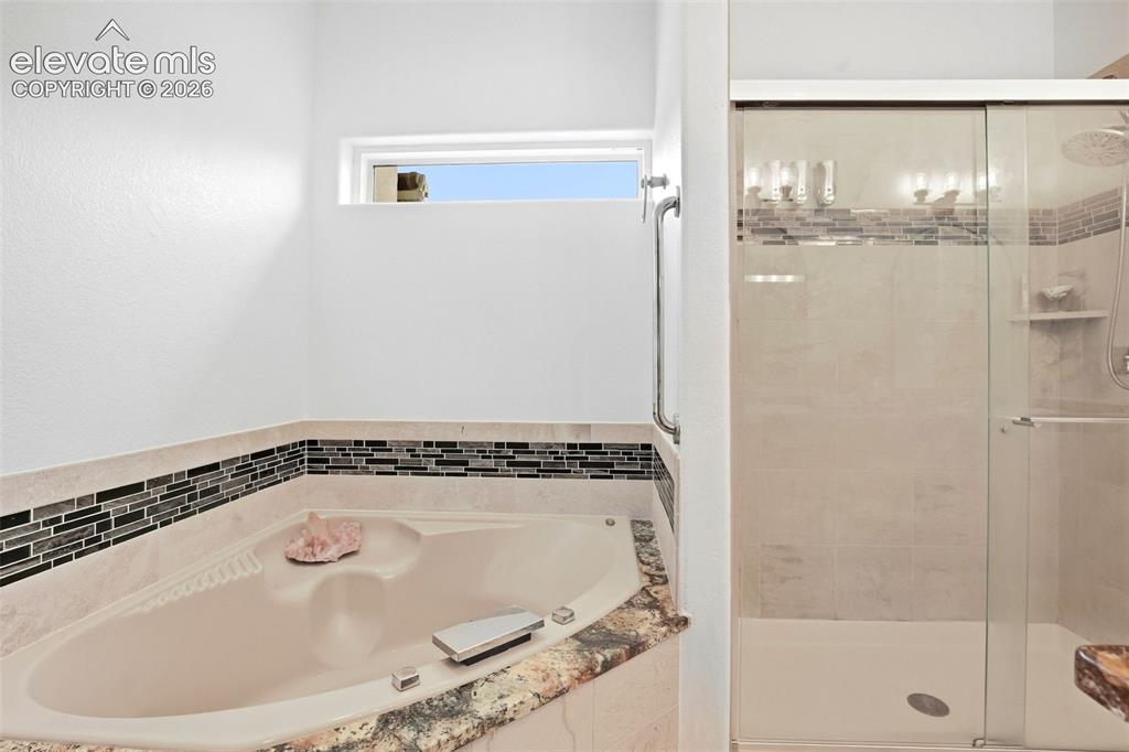 Image 41 of 49: Soaking tub with a natural stone surround and glass mosaic tile accent