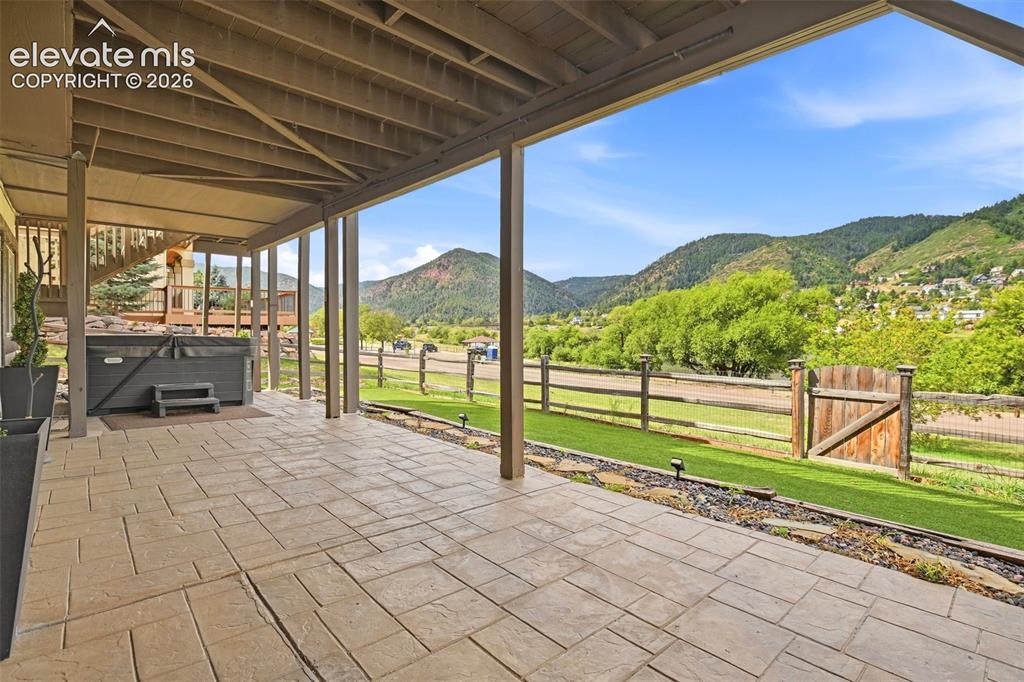 Image 46 of 49: Covered patio with stamped concrete flooring, built-in hot tub, and wood fe