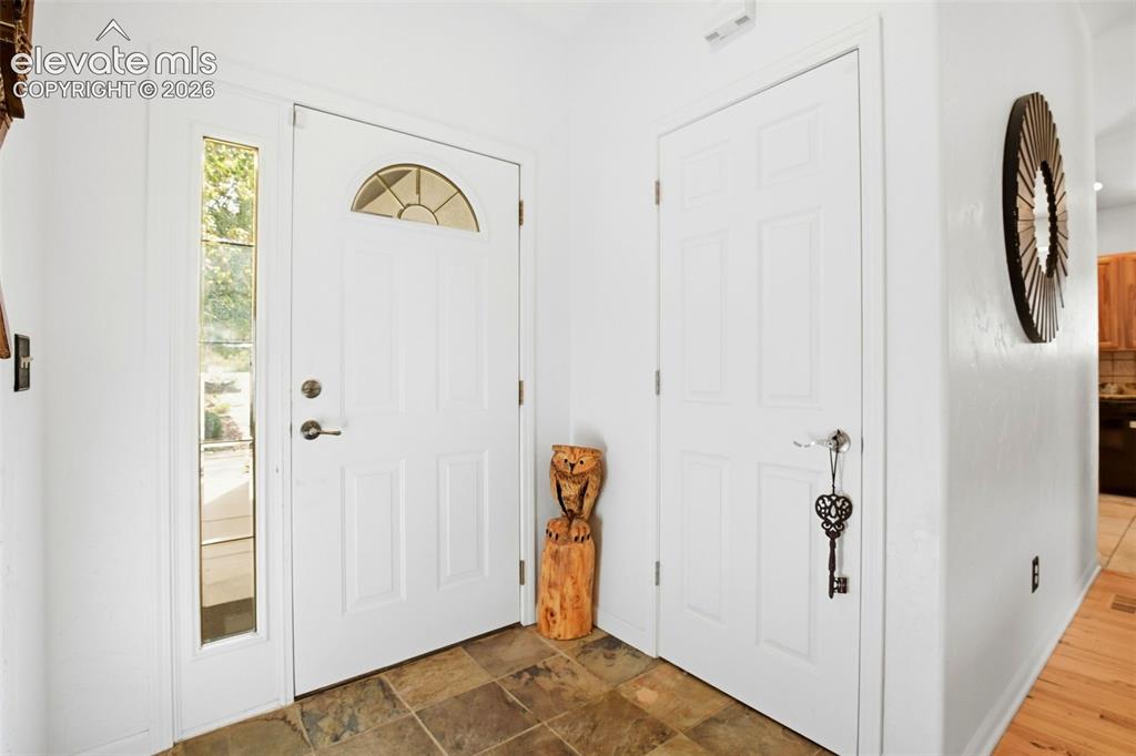 Image 5 of 49: Entryway featuring slate tile flooring, white paneled doors, and a decorati