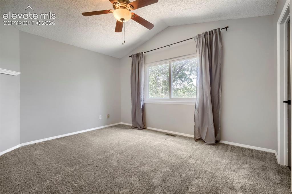 Image 13 of 28: Carpeted room featuring a vaulted ceiling and a ceiling fan