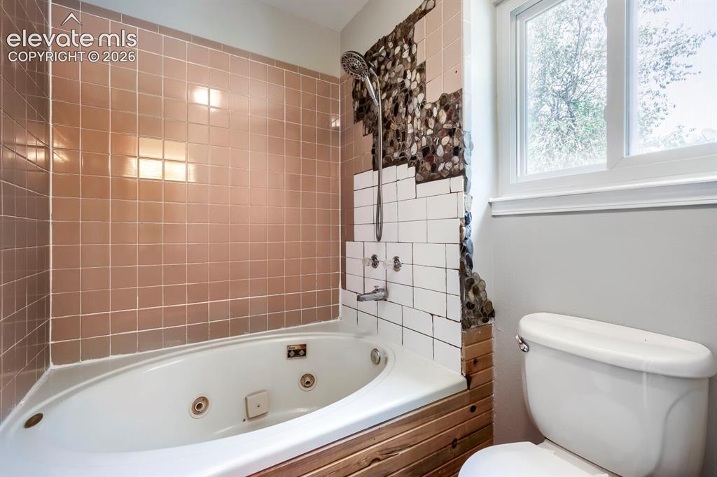 Image 19 of 28: Jetted soaking tub with a tiled surround, complemented by a white toilet an