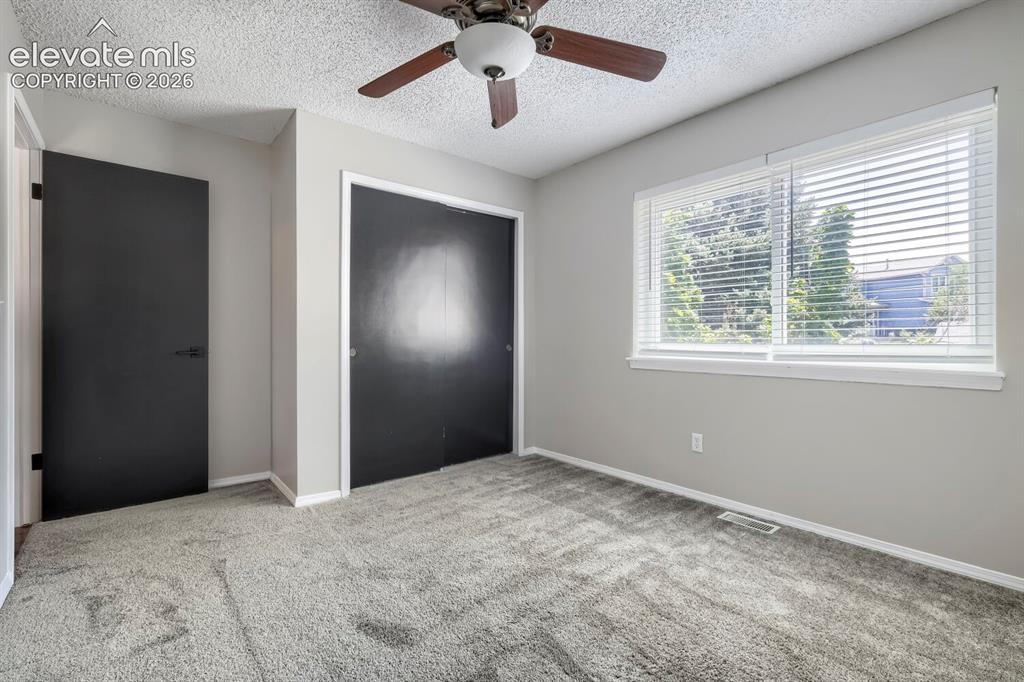 Image 23 of 28: Carpeted room featuring a ceiling fan, two windows with blinds, a solid bla