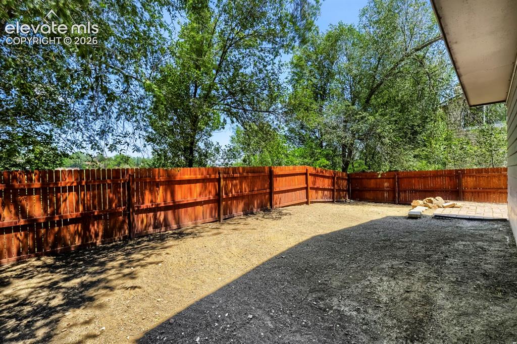 Image 27 of 28: Spacious backyard featuring a full perimeter wooden fence, mature trees, an