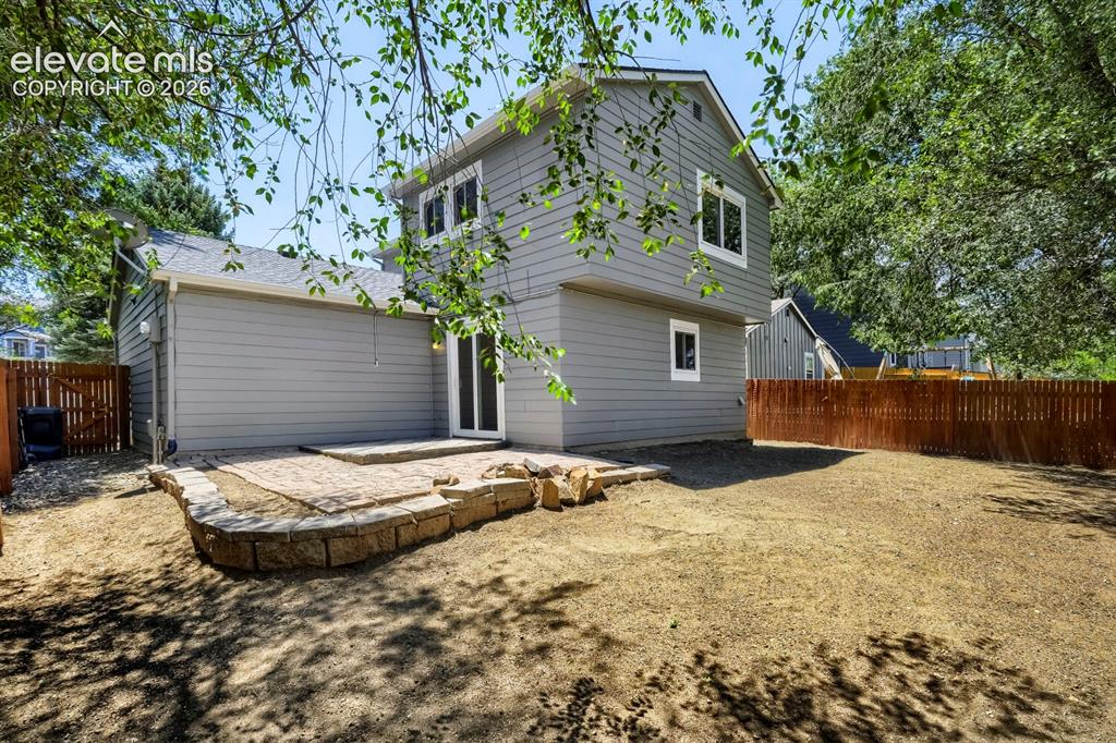 Image 28 of 28: Spacious backyard featuring a paver patio with a stone retaining wall, ligh