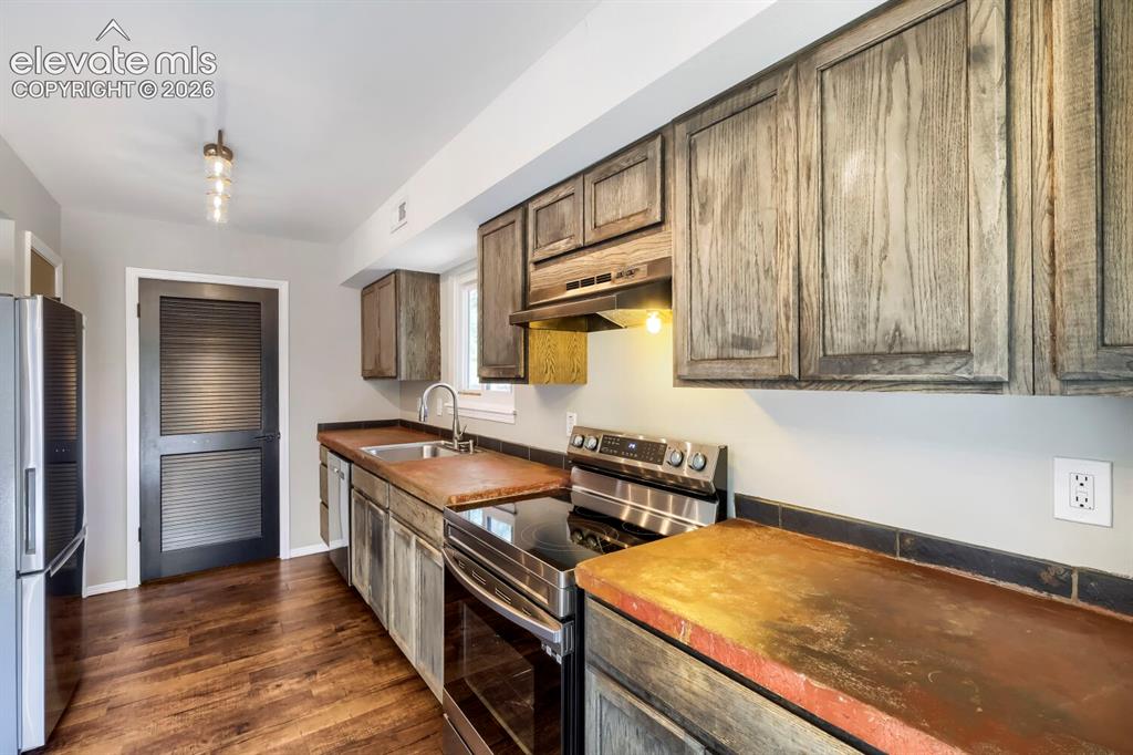 Image 8 of 28: Kitchen featuring wood-finish flooring, stainless steel appliances, dark wo