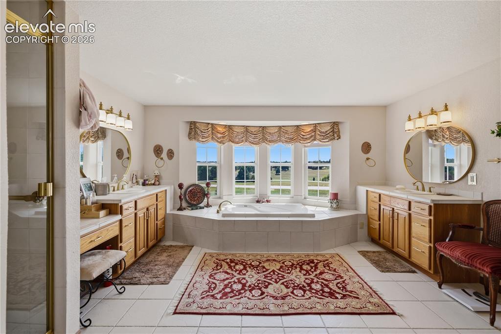 Image 26 of 49: White tile flooring with a large built-in soaking tub, surrounded by a tile