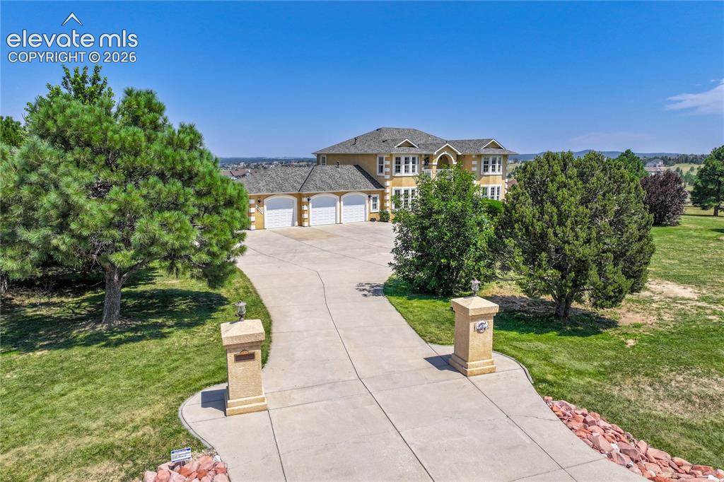 Image 4 of 49: Expansive paved driveway with decorative entry pillars, leading to a multi-