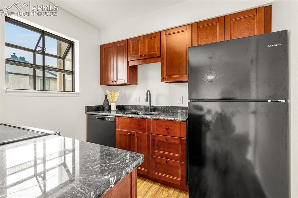 Image 4 of 27: Kitchen featuring black appliances, light wood-type flooring, and dark ston