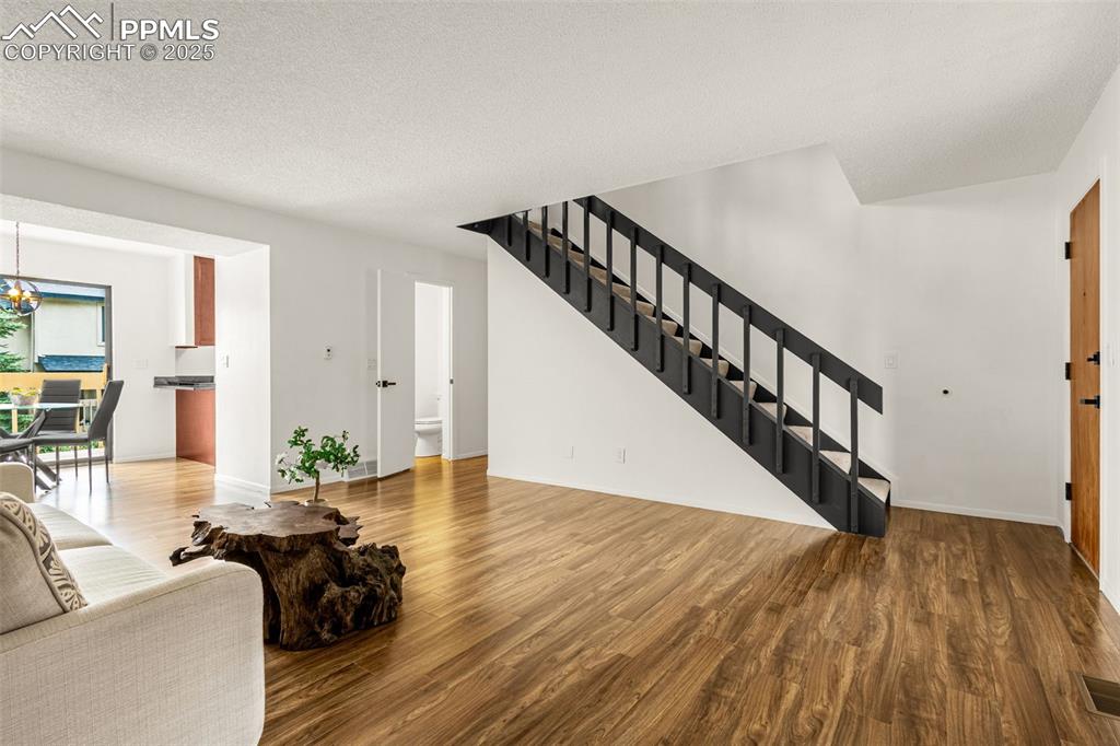 Image 6 of 27: Living area with wood finished floors, stairs, a chandelier, and a textured