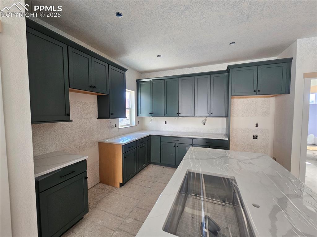 Image 3 of 9: Kitchen with a textured ceiling, electric cooktop, and light stone counters