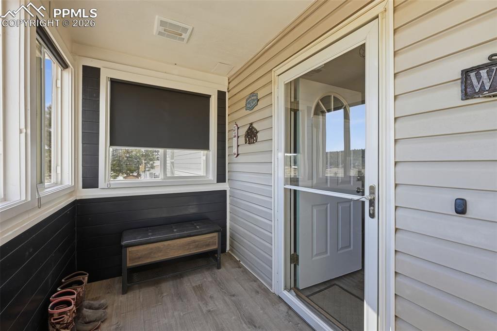 Image 3 of 28: Enclosed entryway featuring light-toned siding, white trim, wood-finish flo