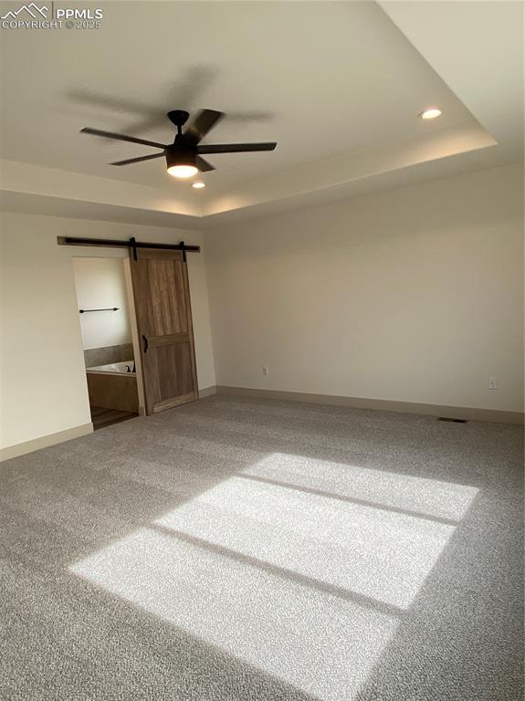 Image 17 of 35: Empty room featuring a tray ceiling, a barn door, carpet floors, ceiling fa