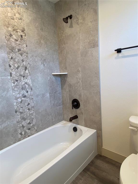 Image 28 of 35: Bathroom with dark wood finished floors and bathtub / shower combination
