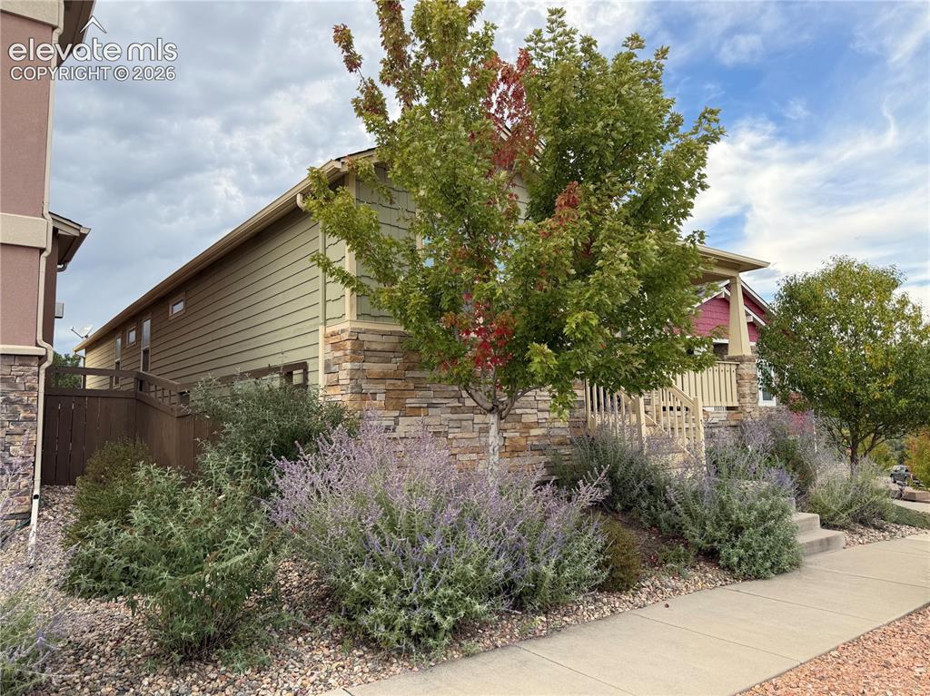 Image 2 of 6: Exterior siding with stone accents, mature trees, and established shrubbery