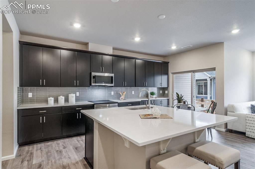 Image 2 of 25: Kitchen with backsplash, light stone counters, a kitchen bar, appliances wi