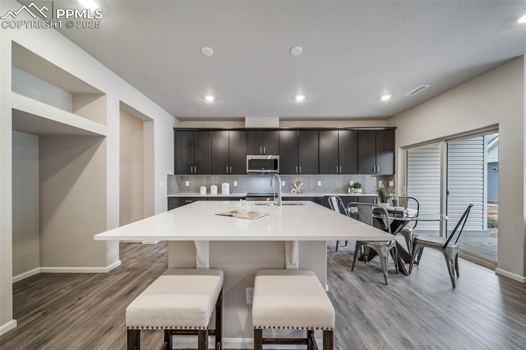Image 8 of 25: Kitchen featuring decorative backsplash, an island with sink, a breakfast b