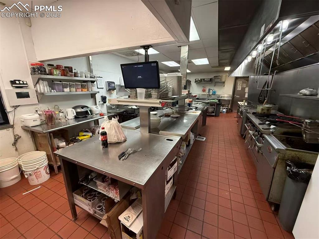 Image 6 of 10: Kitchen with stainless steel counters, a paneled ceiling, and wall chimney