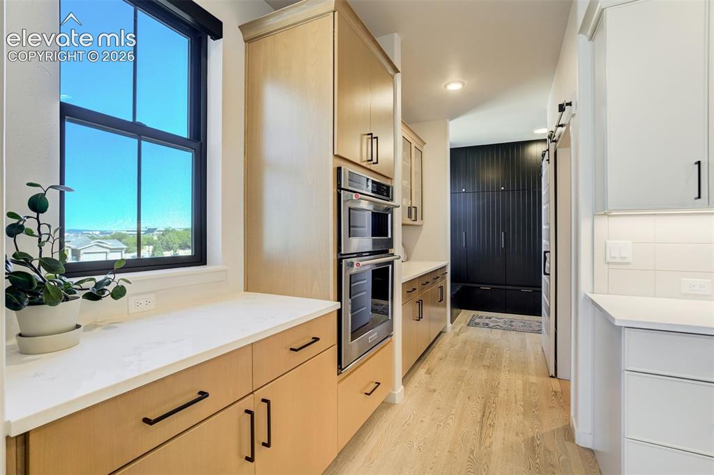 Image 15 of 50: Modern kitchen corridor featuring built-in double ovens, light wood-finish