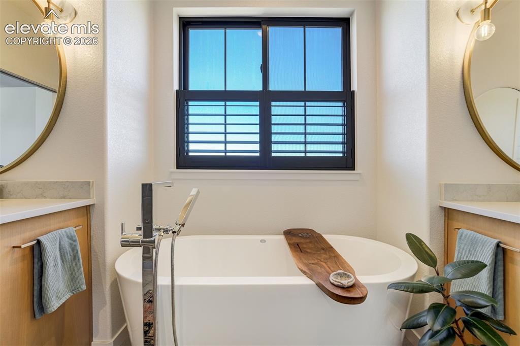 Image 26 of 50: Freestanding soaking tub with a floor-mounted chrome faucet, flanked by dua