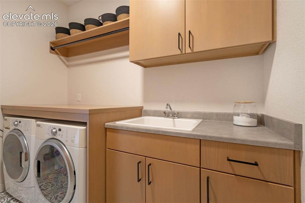 Image 34 of 50: Laundry area featuring light wood-finish cabinetry, a built-in sink with a