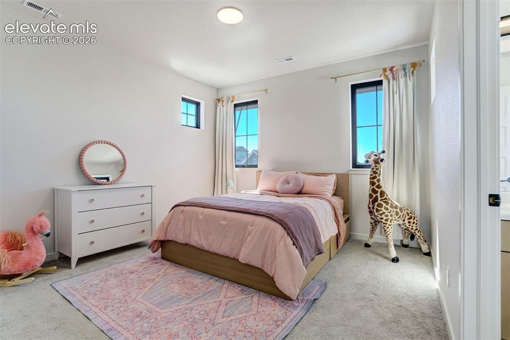 Image 35 of 50: Bright bedroom featuring soft gray carpet flooring, white walls, and a cont