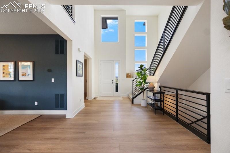 Image 10 of 49: Entrance foyer with light wood-style floors, baseboards, and a towering cei