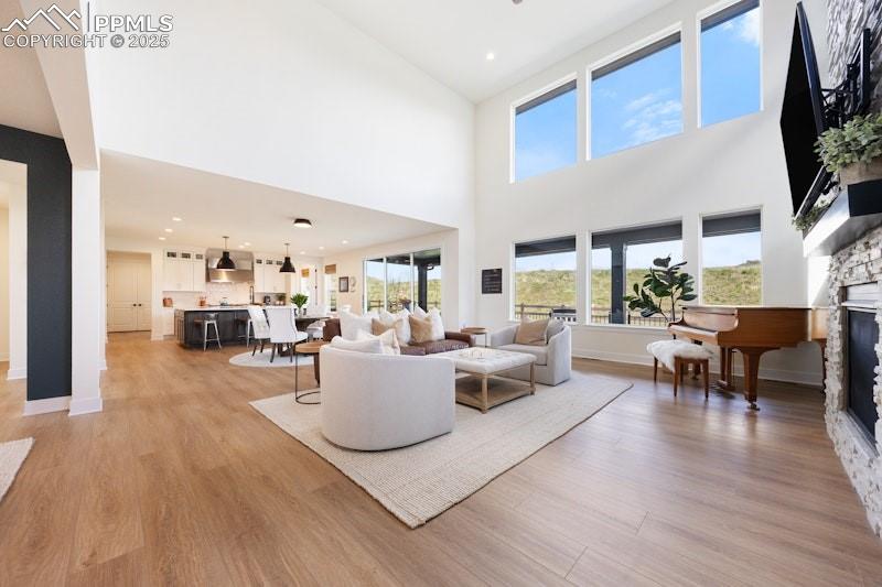 Image 14 of 49: Living area with a fireplace, light wood-type flooring, a towering ceiling,