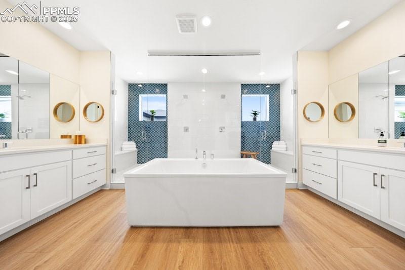 Image 26 of 49: Bathroom featuring wood finished floors, a freestanding bath, and two vanit