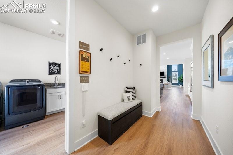 Image 39 of 49: Hallway with washer / dryer, light wood-style flooring, baseboards, a sink,