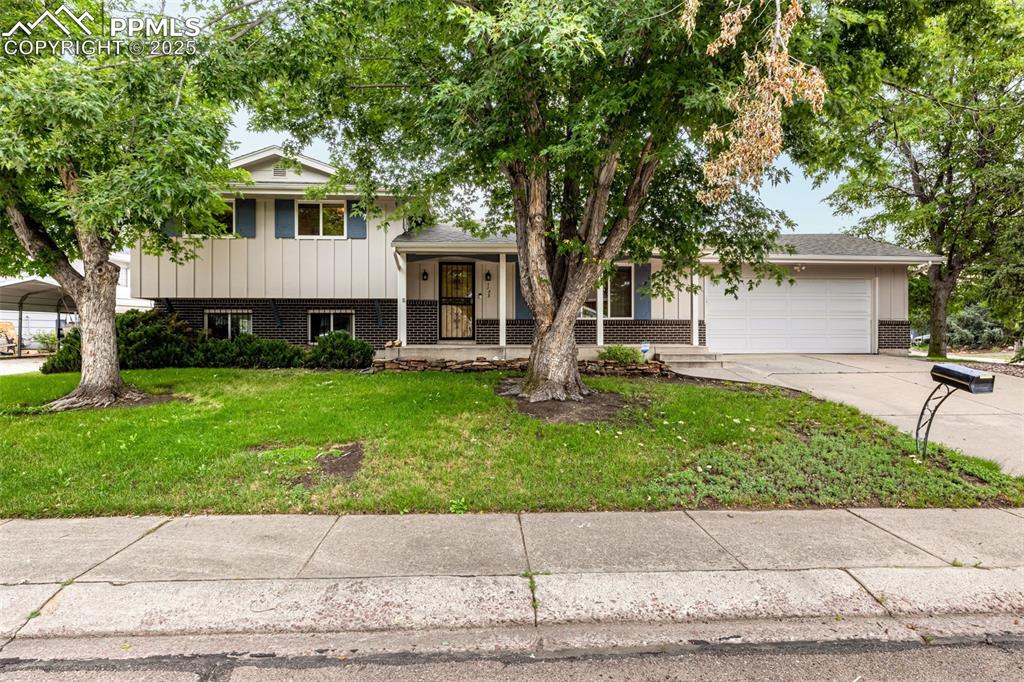 Caption: Split level home with brick siding, covered porch, a front lawn, driveway, and an attached garage