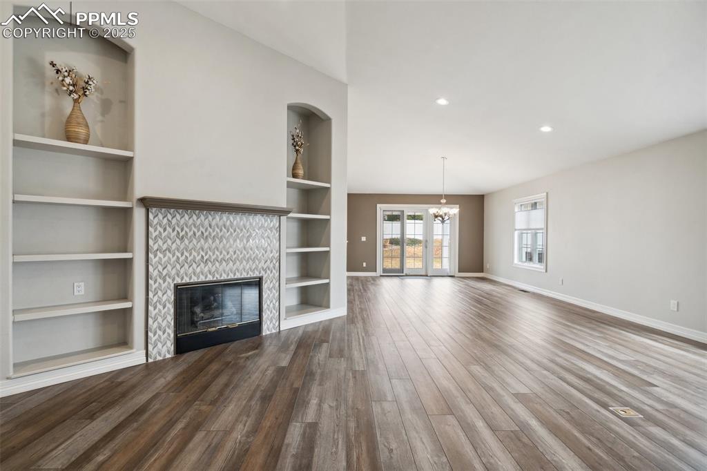 Image 4 of 49: Unfurnished living room with a tiled fireplace, a chandelier, wood finished