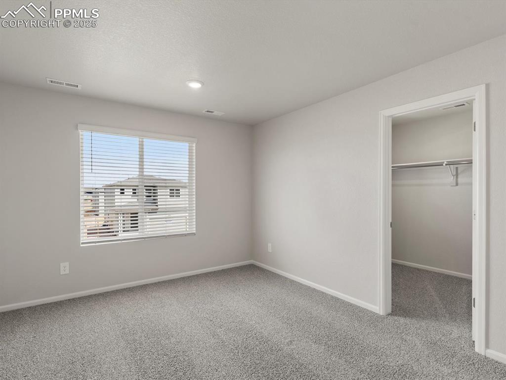 Image 16 of 30: Unfurnished bedroom with a walk in closet, light colored carpet, and a text